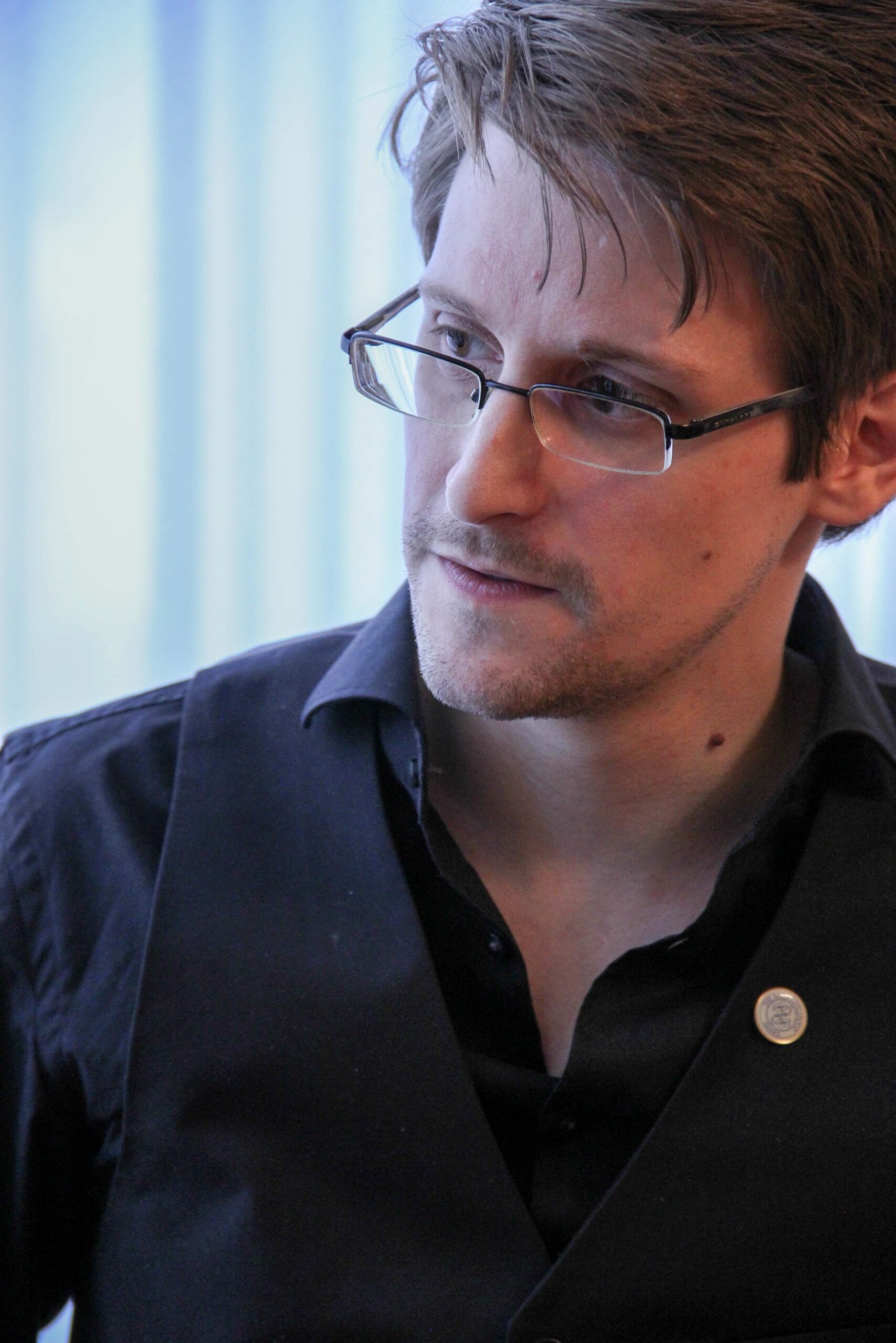 Edward Snowden, 2014 Right Livelihood Laureate, in glasses and a dark shirt, looking to one side against a pale blue backdrop.