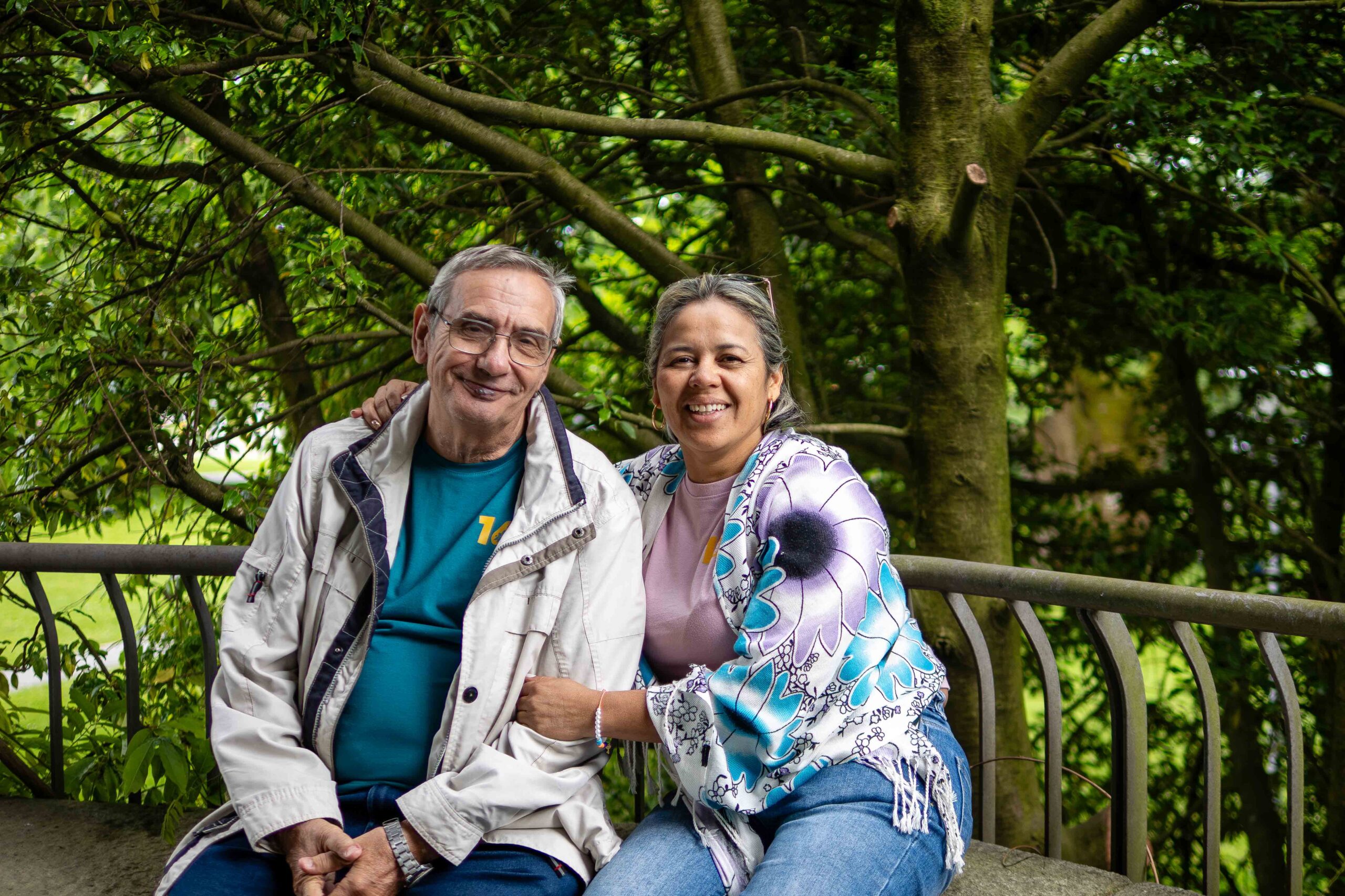 Georg and Yadira, representatives of Cecosesola, sitting and facing the camera, against some trees in the background.