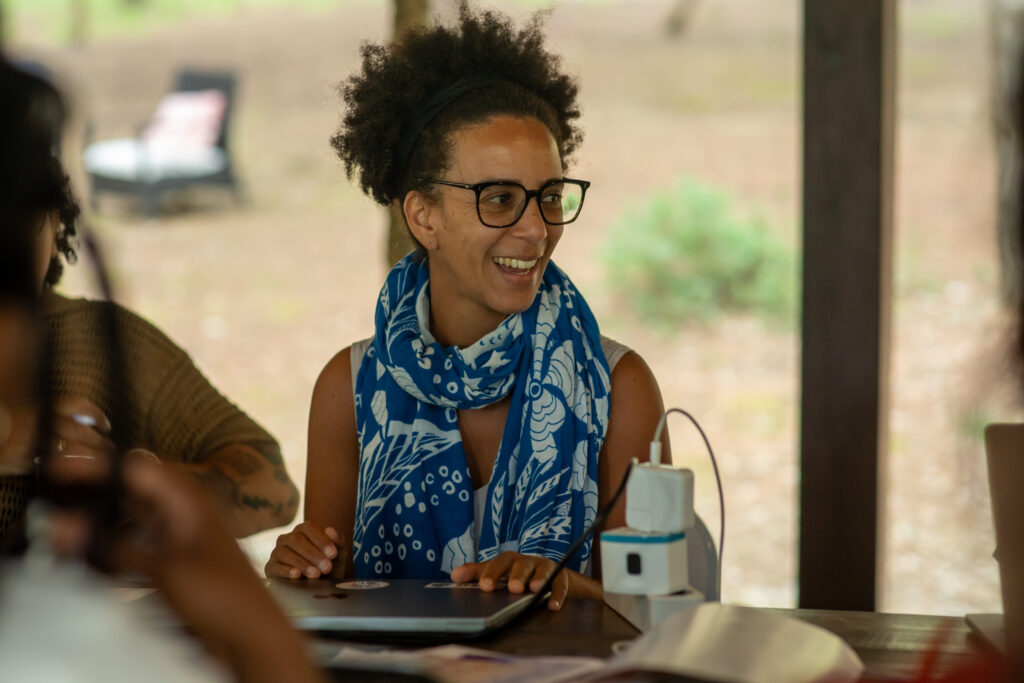 2026 Right Livelihood Laureate Timnit Gebru sitting at a table DAIR seminar, laughing.