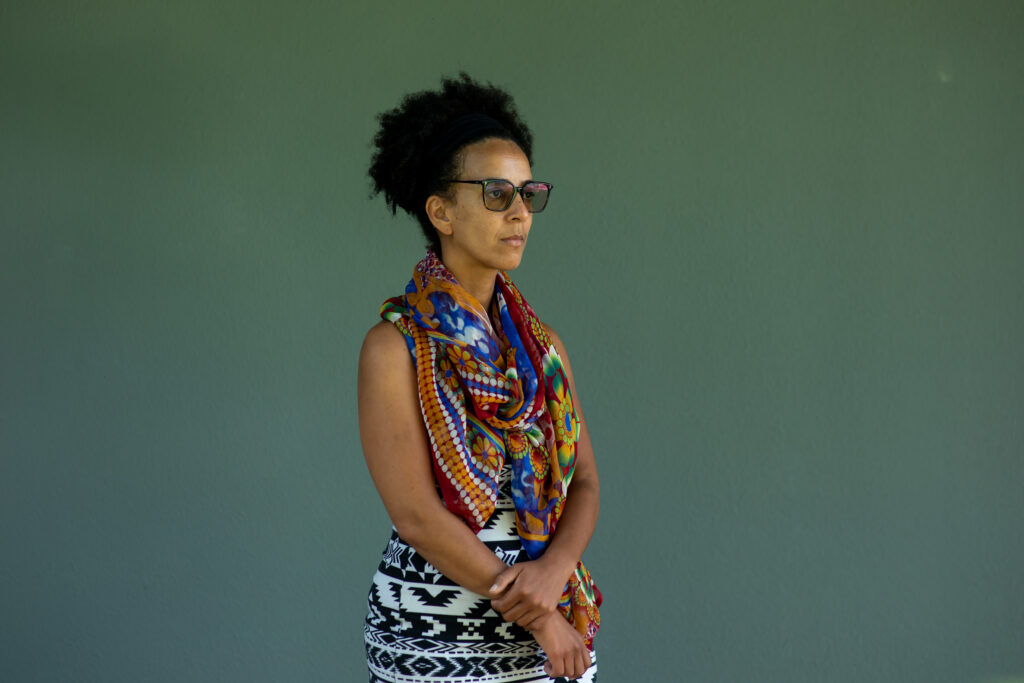 2026 Right Livelihood Laureate Timnit Gebru looking off to the side in front of green wall.